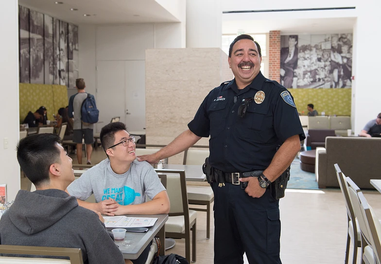 A Police officer smiling and talking to two college students