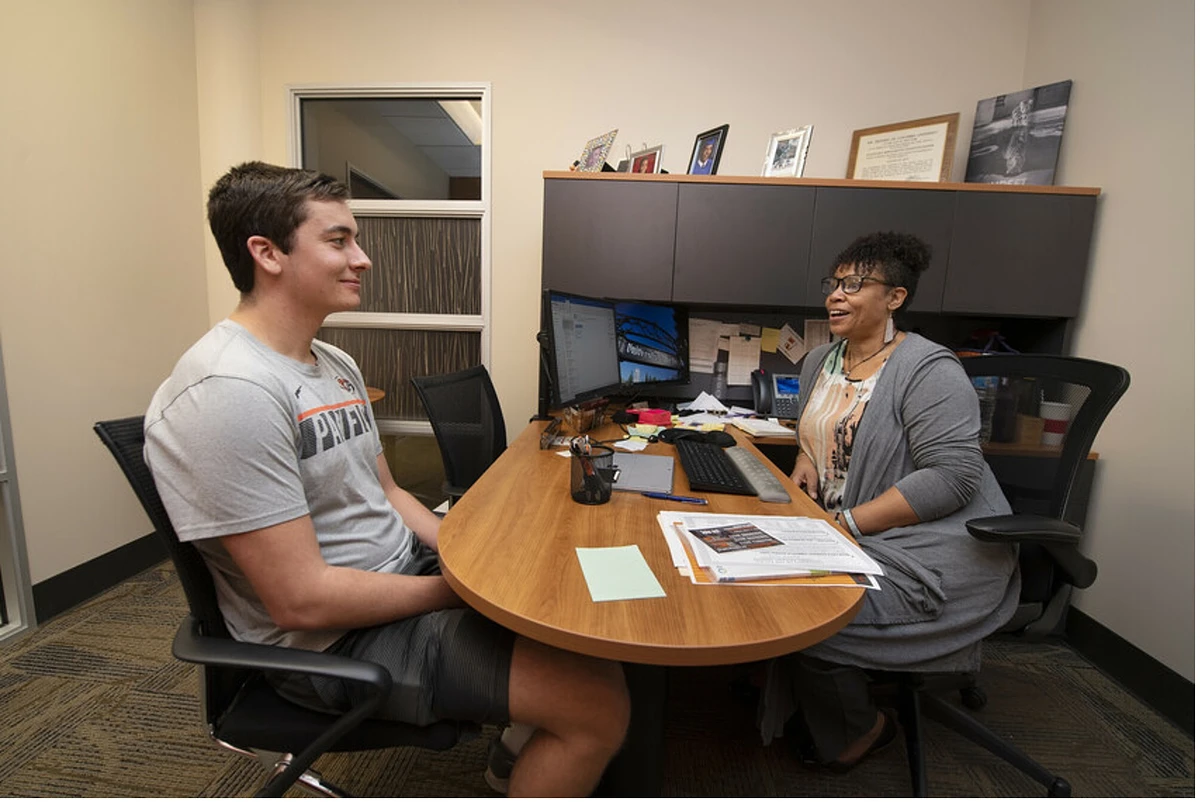 A college student with his faculty mentor inside an office.