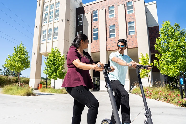 Two college students on scooters in front of dormitories
