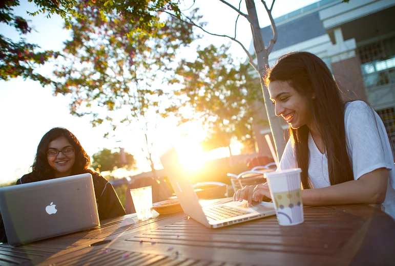 Two college students sitting outside with laptops