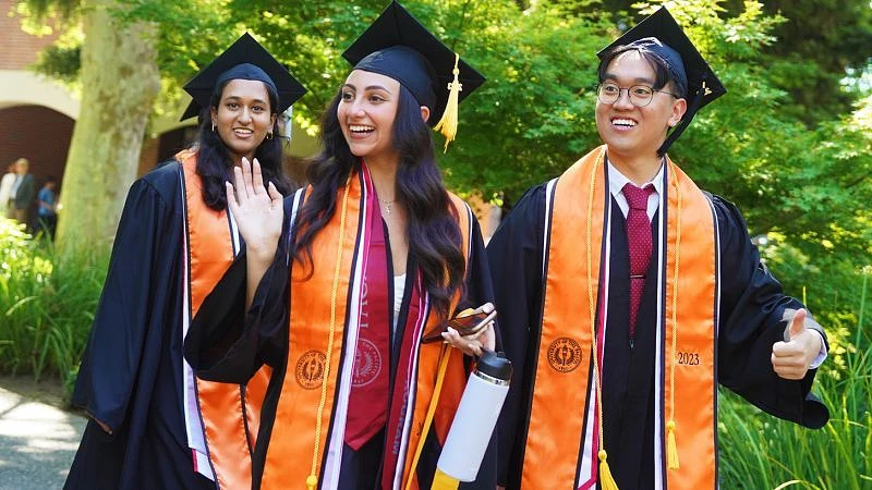 Smiling students waving in commencement attire 